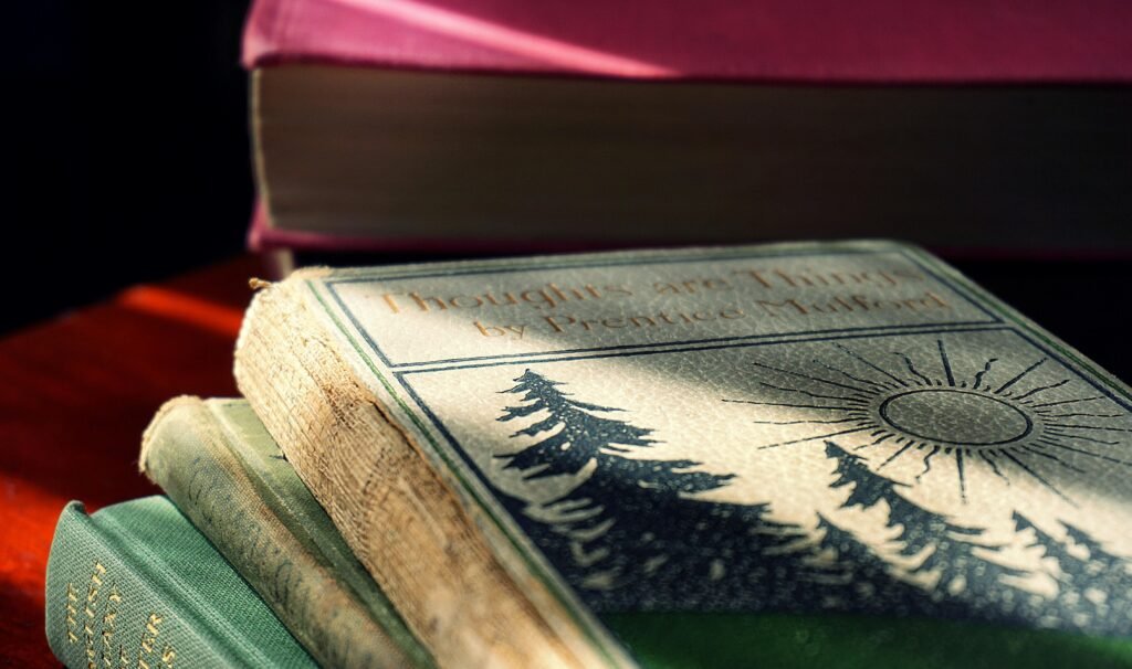 Close-up of vintage hardcover books stacked on a wooden table with sunlight casting shadows.